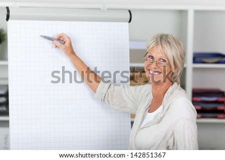 Portrait of happy senior businesswoman pointing with felttip pen on presentation board at office