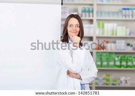 Portrait of confident female pharmacist standing by flipchart in pharmacy