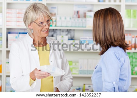 Senior female pharmacist giving prescribed medicine to customer in pharmacy