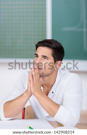 Thoughtful young male student with hands clasped looking away in classroom