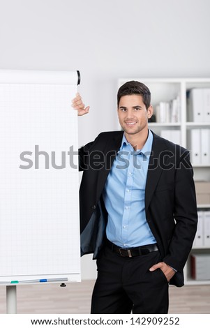 Portrait of confident young businessman with hand in pocket standing by flip chart in office