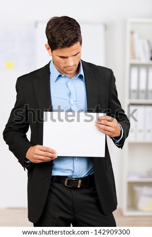 Young businessman holding a blank white paper and looking down.