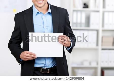Smiling young well dressed businessman showing a blank sheet.
