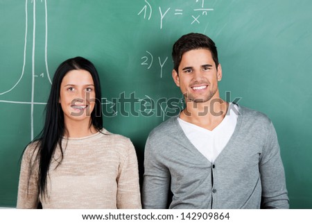 Male and female students standing in front of the blackboard inside a classroom.