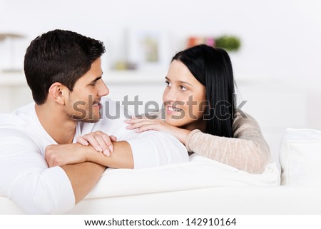 Romantic young couple relaxing on a sofa at home looking into each others eyes with tenderness and love
