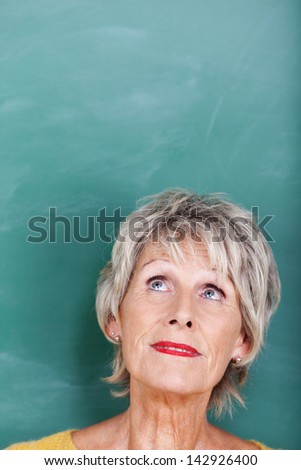 Closeup of thoughtful senior teacher looking up against chalkboard