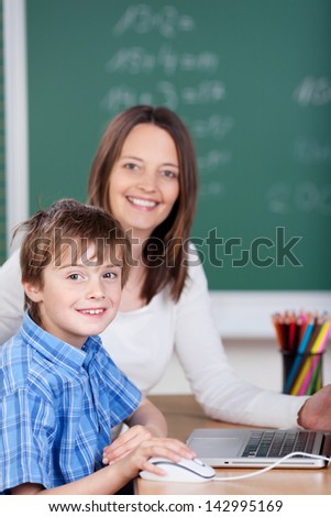 Teacher teaching young cheerful student from laptop in the classroom