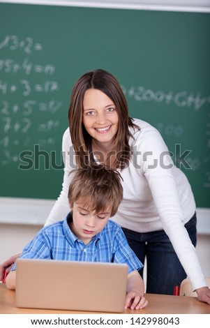 Teacher teaching young student from laptop in the classroom