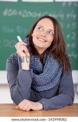 Smiling teacher looking up while holding a chalkboard at the classroom