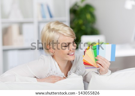 Happy blond young woman holding color samples while sitting on couch at home