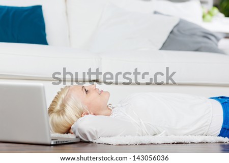 Side view of a thoughtful and happy blond woman with laptop relaxing on the floor at home