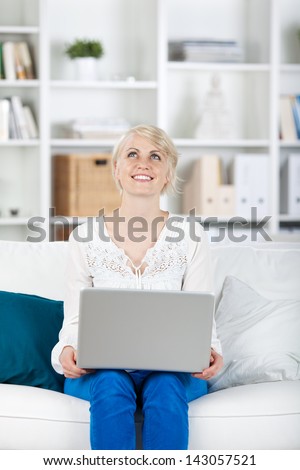 portrait of a happy woman with laptop on sofa looking up