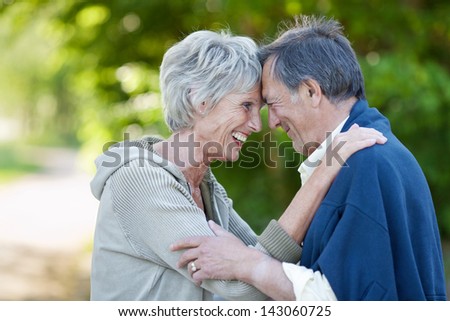 Profile shot of happy loving senior couple with head to head smiling in park