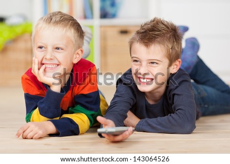 Happy brothers with remote control watching television while lying on hardwood floor