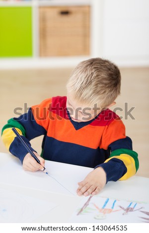 Little boy drawing on paper at table in house