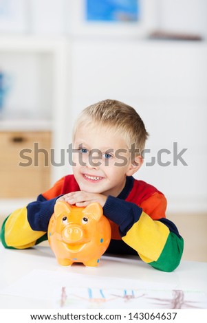 Portrait of happy little boy with piggybank at table in house