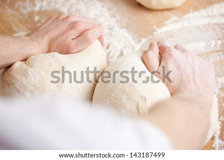 Baker kneading bread dough with one portion for a loaf under each hand
