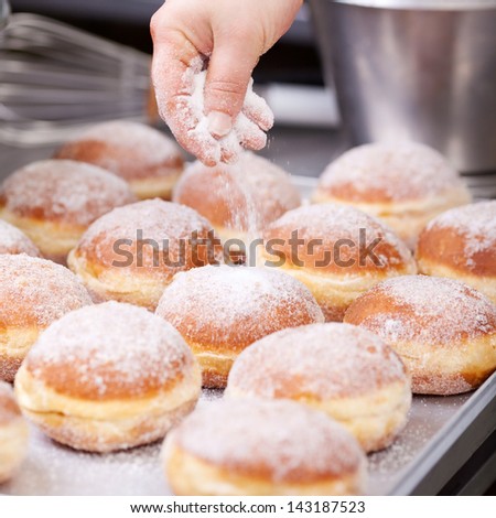 Baker pours sugar over pastry on a bakery tray