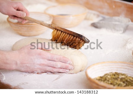 Glazing uncooked bread with a brush in order to get the seeds and kernels used as garnish to adhere to the top