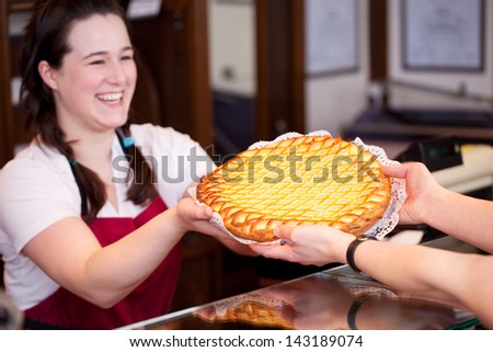 Bakery worker selling a freshly baked golden apple tart handing it to a customer over the counter