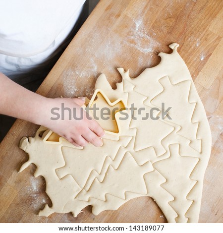 Baker cutting Christmas buscuits in the shape of Christmas Trees from a portion of rolled pastry, overhead view showing the cutouts