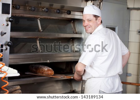 Friendly male chef or baker removing a loaf of freshly baked bread from the oven in the bakery