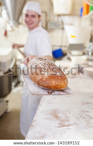 Baker carrying a gourmet loaf of fresh baked bread that he has just removed from the oven