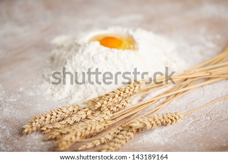 Ingredients for a loaf of fresh baked bread in a bakery with a bunch of ripe golden wheat lying alongside a pile of flour with a fresh egg broken into the top