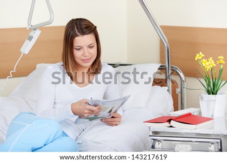 Photo of a young female patient reading a newspaper while lying on the bed in hospital