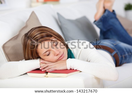 Woman Relaxing And Sleeping On Her Book As She Lies On A Sofa Enjoying A Lazy Day