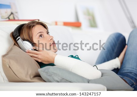 Woman listening to music relaxing on the sofa lying on her back wearing headphones concentrating on the soundtrack