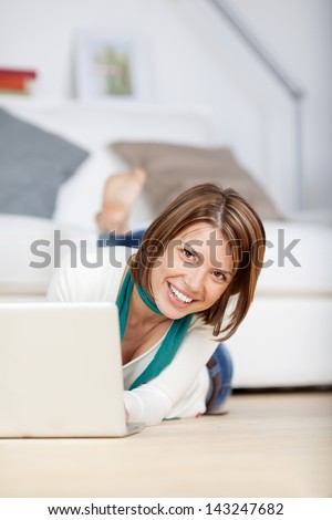 Image of a smiling young woman working on the laptop and giving a smile for the camera.