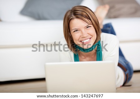 Image of a cheerful female looking at the camera while working on the laptop in the living room.