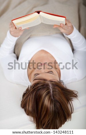 Photo of a young female lying in bed and reads a book.