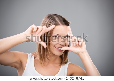 Smiling female posing with a hand sign on grey background