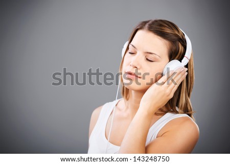 Cheerful woman feel the music through headset on grey wall background
