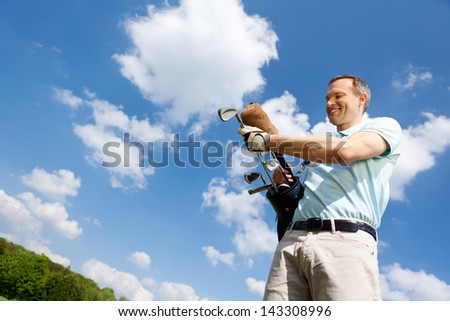Low angle view of mature man removing golf club against sky