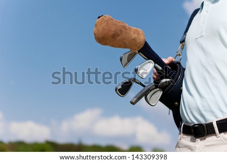 man carrying golf clubs in bag against blue sky