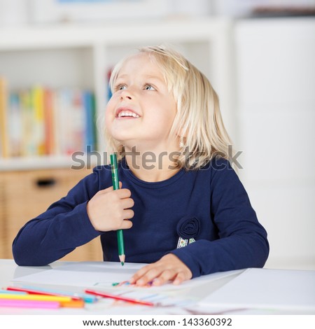 Thoughtful little girl holding color pencil while drawing at table in house