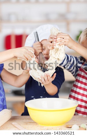 Little girl using whisk on dough while siblings holding it at kitchen counter