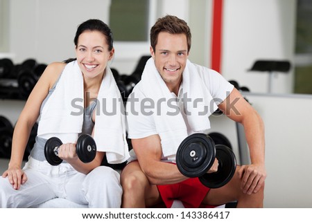Portrait of happy young couple lifting dumbbells in gym