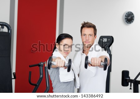 Healthy couple holding dumbbells in the gym with towel around their neck