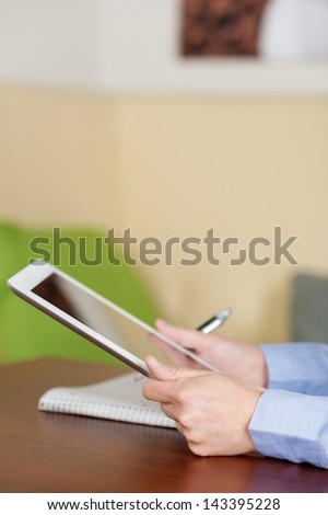 Woman at the coffee shop holding a tablet and taking notes in a paper notebook