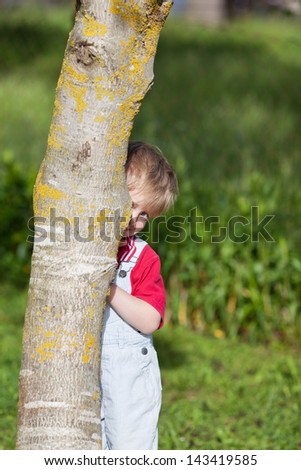 Portrait of cute boy hiding behind tree trunk in yard