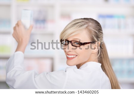 Friendly and smiling female pharmacist stores the medicines in the pharmacy shelves