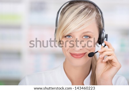 Portrait of a friendly female pharmacist looking at camera using headsets and holding the microphone