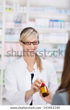Friendly and smiling female pharmacist gives a bottle of pills to a patient