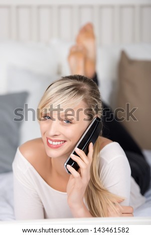 Smiling female calling through telephone in the bedroom