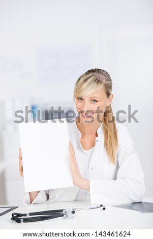 Smiling female doctor sitting and showing blank paper
