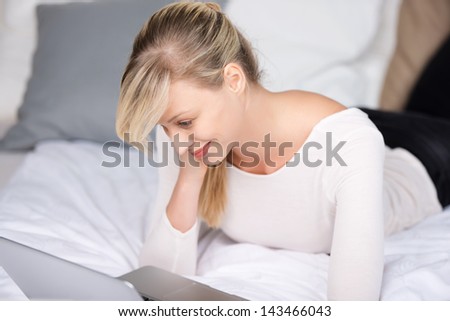 Blond cheerful female surfing the internet at her bedroom